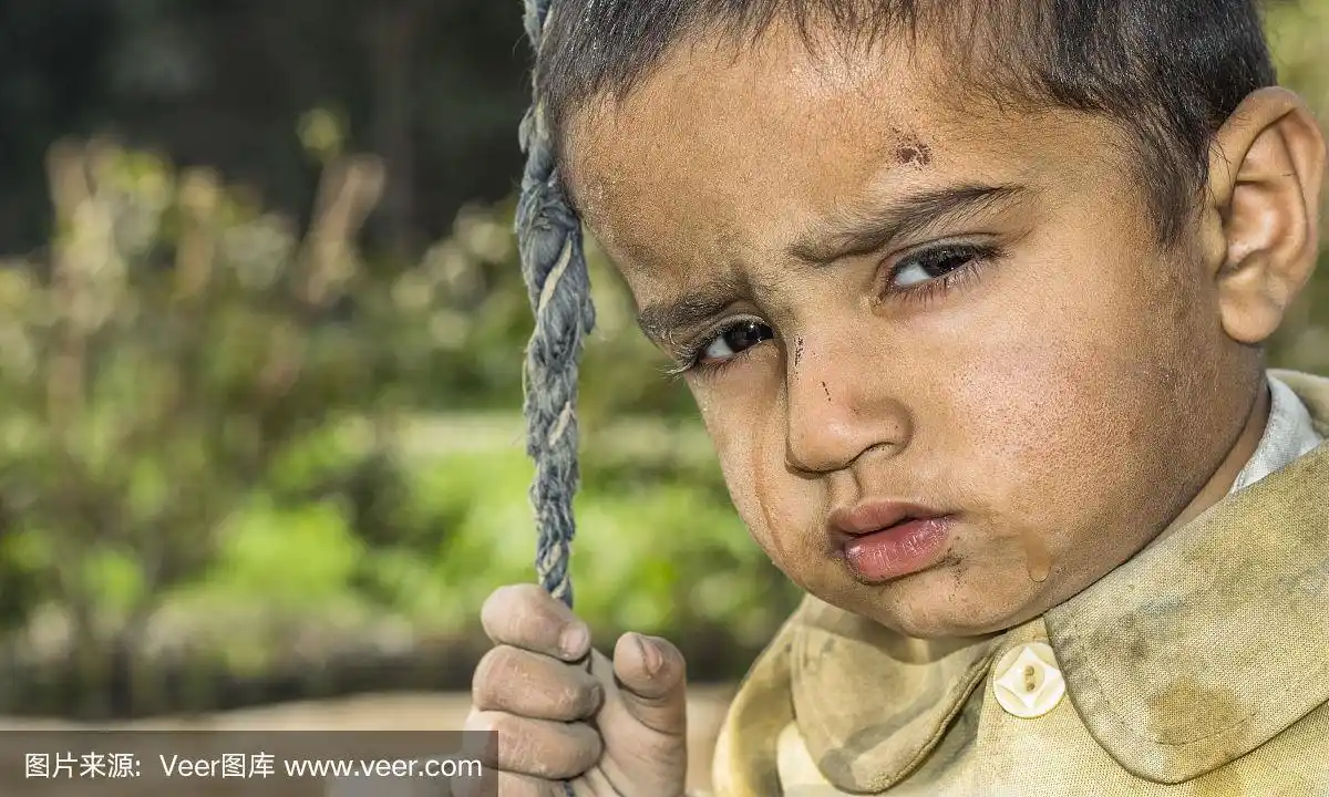 一个贫穷的盯着饥饿的孤儿男孩在难民营的特写,他的脸上有悲伤的表情