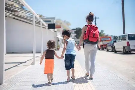 单亲妈妈带着两个孩子走在海滨避暑山庄,在温暖的阳光下,手牵着手从