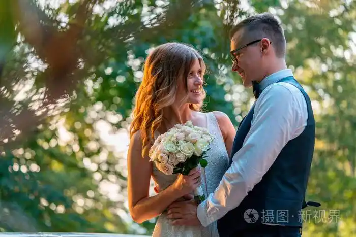 新婚夫妇紧紧地站在一起微笑着拥抱着日落的公园背景模糊