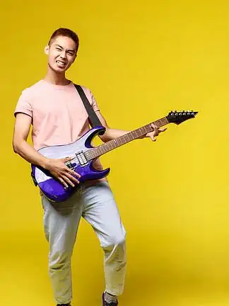 时髦英俊的亚洲 i>男 /i> i>人 /i>弹电吉他的垂直肖像,微笑着高兴,在