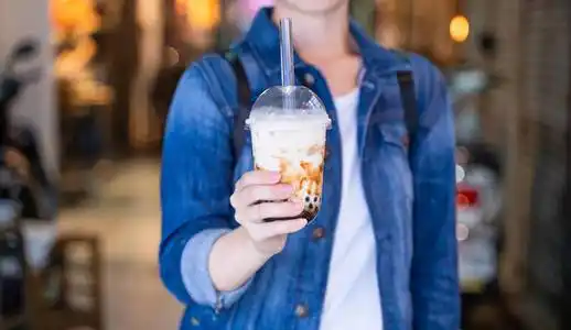 在台湾夜市,年轻女子拿着,喝着红糖味的木薯珍珠泡奶茶照片