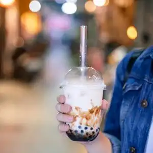 红糖茶在台湾夜市,年轻女子拿着,喝着红糖味的木薯珍珠泡奶茶照片