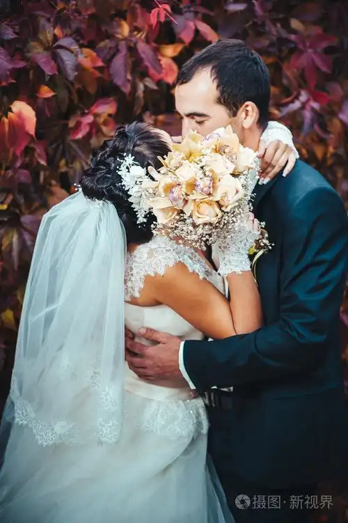 接吻的结婚礼服的年轻夫妇.新娘控股束鲜花