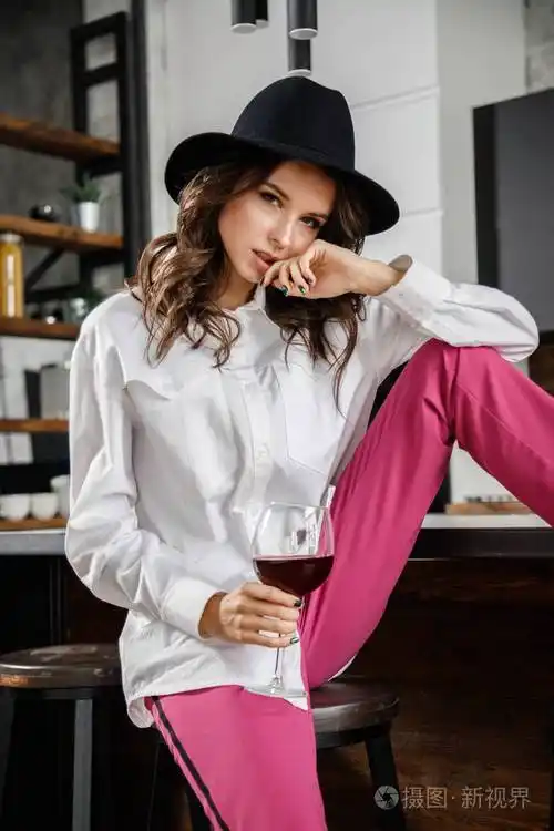 时尚肖像美女黑发模特穿白色衬衫和粉红色裤子在豪华公寓内部摆姿势的