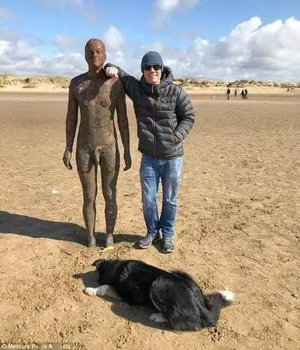 沙滩上,牧羊犬把球叼给了一个雕像,然后