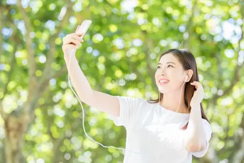 树下用手机听音乐的甜美女生