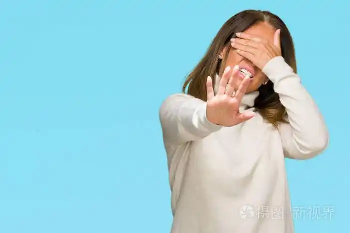 美丽的中年成年妇女穿着冬季毛衣,在孤立的背景上用手遮住眼睛,用悲伤